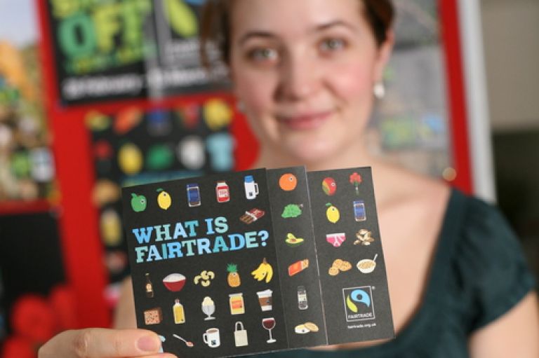 Woman holds up Fairtrade flyer showing a variety of food products with Fairtrade stickers on them
