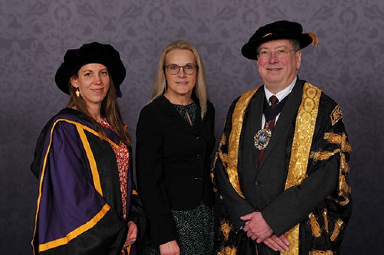 Prof Katrin Hohl, Lord Mayoress and Lord Mayor dressed in formal wear against a plain grey backdrop.