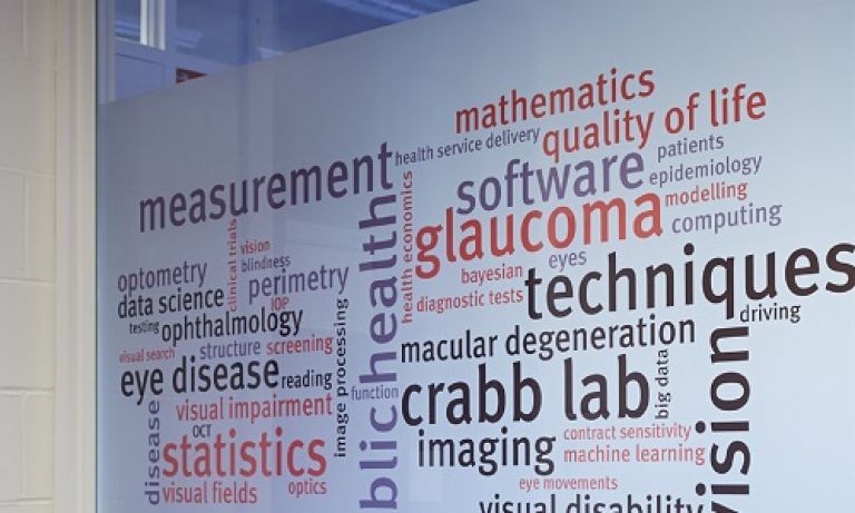 Window of the Crabb Lab office with a word cloud image on it comprised of words related to the lab's research like 'measurement' and 'glaucoma'