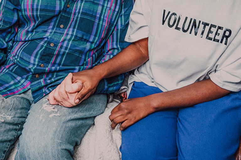 A woman wearing a top with 'VOLUNTEER' written across the chest, sitting on a sofa with a man and holding his hand.