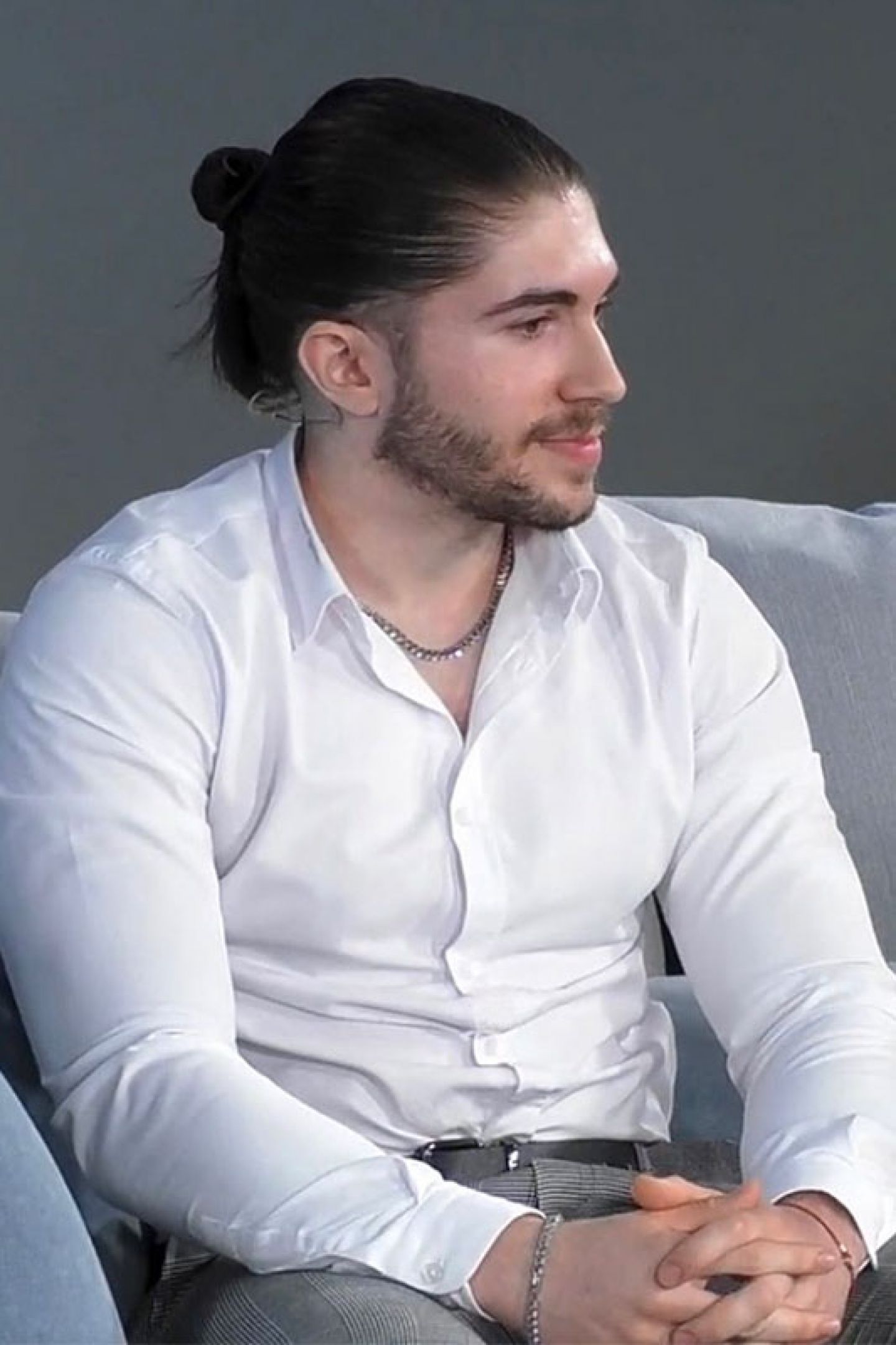 Portrait of student Rosen Georgiev, BSc Computer Science, wearing a white collared shirt and grey work trousers sitting on a grey couch