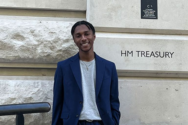 Picture of student Miles Johnson wearing a blue suit in front of the building of the HM Treasury
