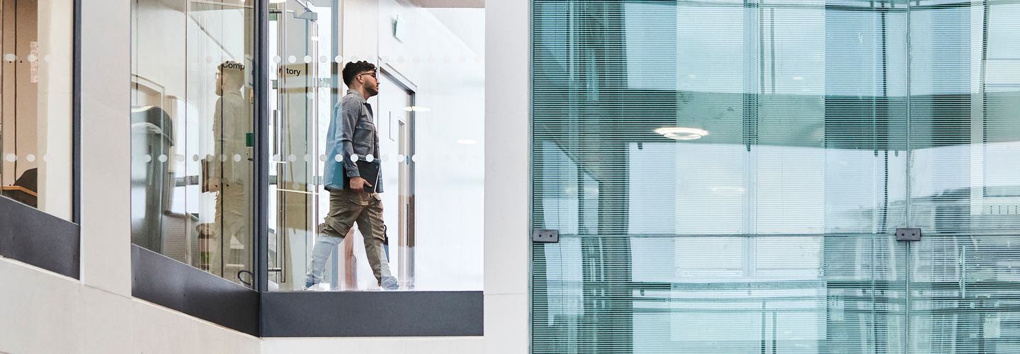 Student walking through the modern glass walled corridors of Rhind building.