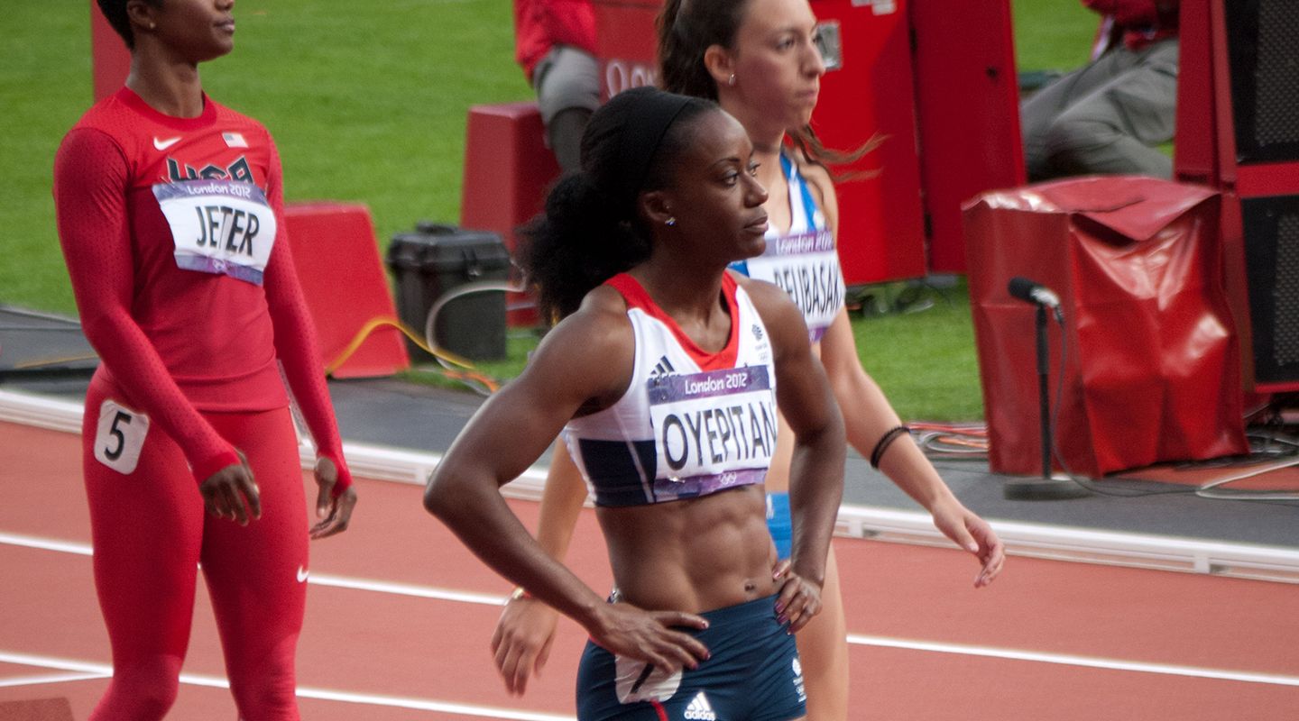 Abiodun Oyepitan in racing kit, standing at the starting point of a race track with other sportswomen.