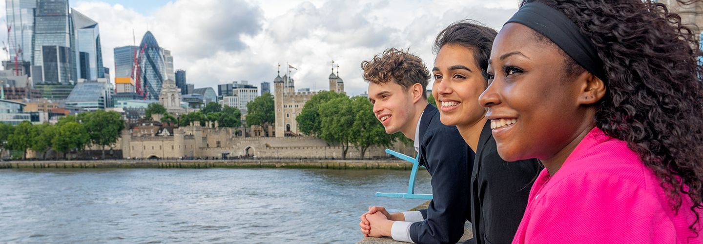 Diverse group of Bayes students standing on the Tower Bridge, looking over at the river Thames. Visible behind them is The Tower of London, as well as the City of London.