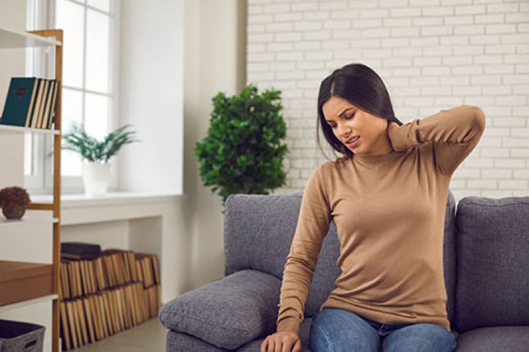 Woman sitting on a sofa holding her neck in pain.