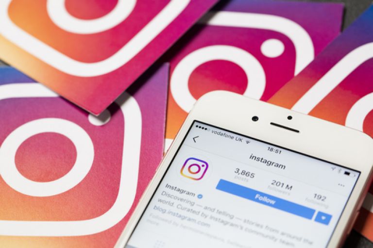 An image of a phone with the instagram app open to create an account. In the background the pink/purple square Instagram logo appears a few times