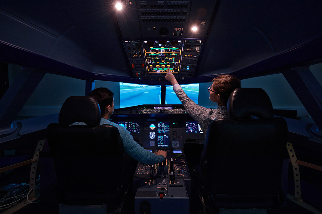 Two students inside a Airbus A320 flight simulator touching upper overhead panel