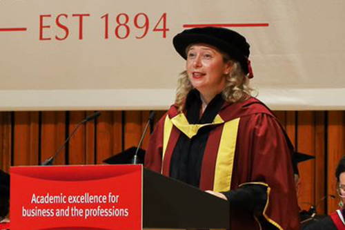Professor Caroline Wiertz standing behind a lectern in graduation gown and hat