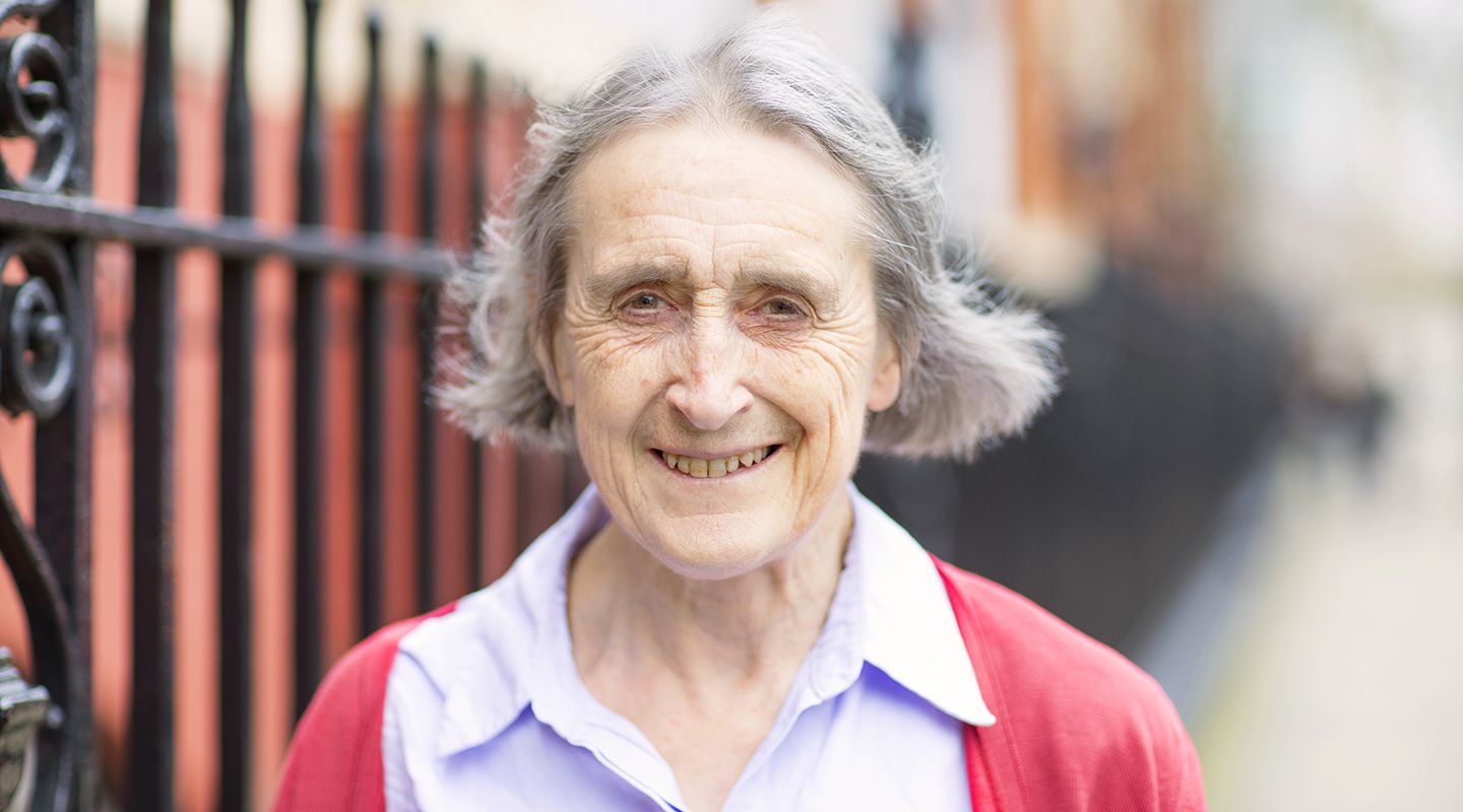 Alison Macfarlane, an older lady with chin length grey hair, smiling as she walks down a street.