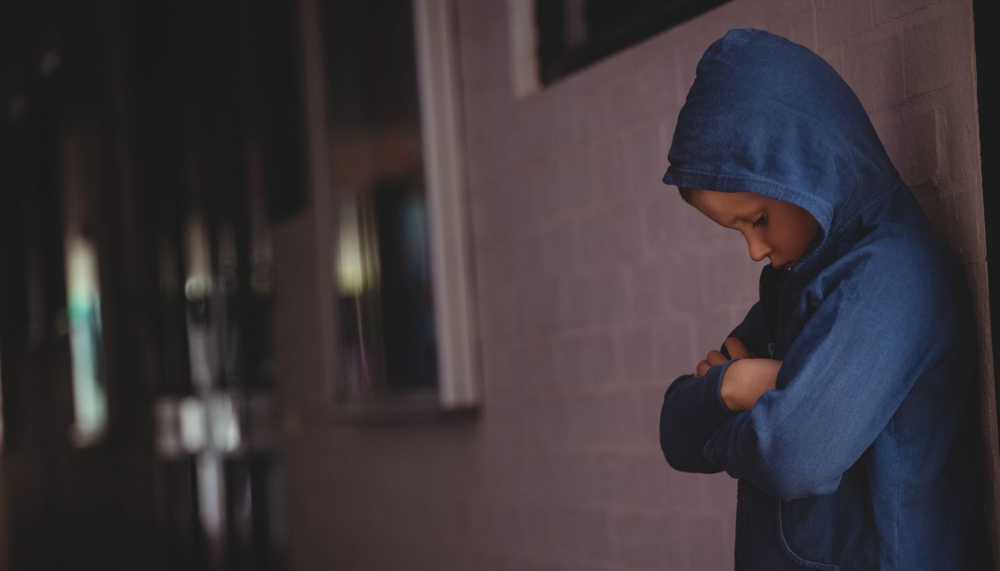 Young boy in blue raincoat looking sad.