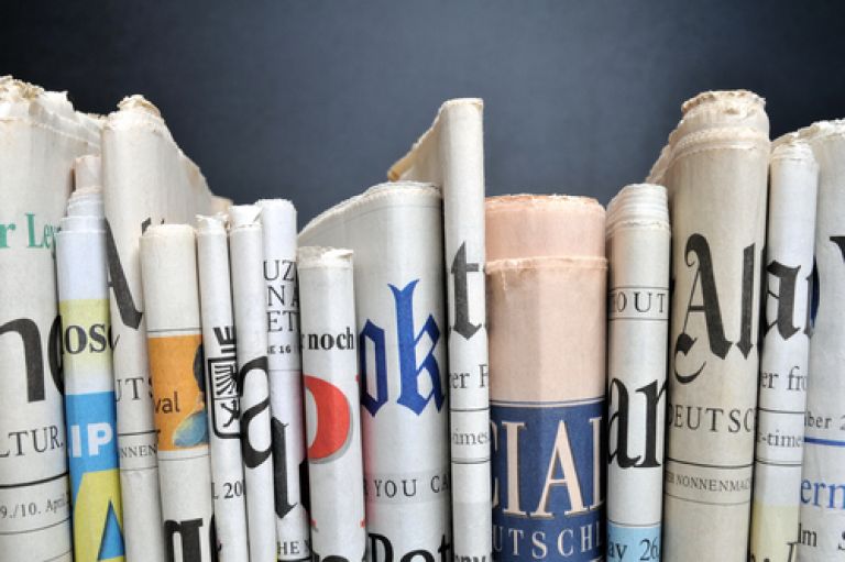 An image of a row of newspapers folded. We can only see the folded spine of paper. 