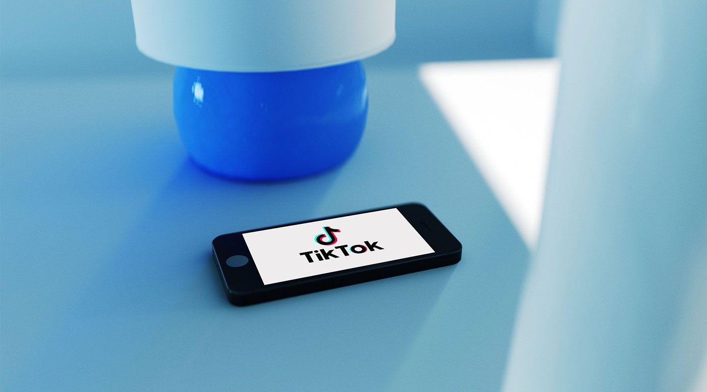 Image of a phone with the TikTok logo on its screen, against a blue background with a blue lamp.