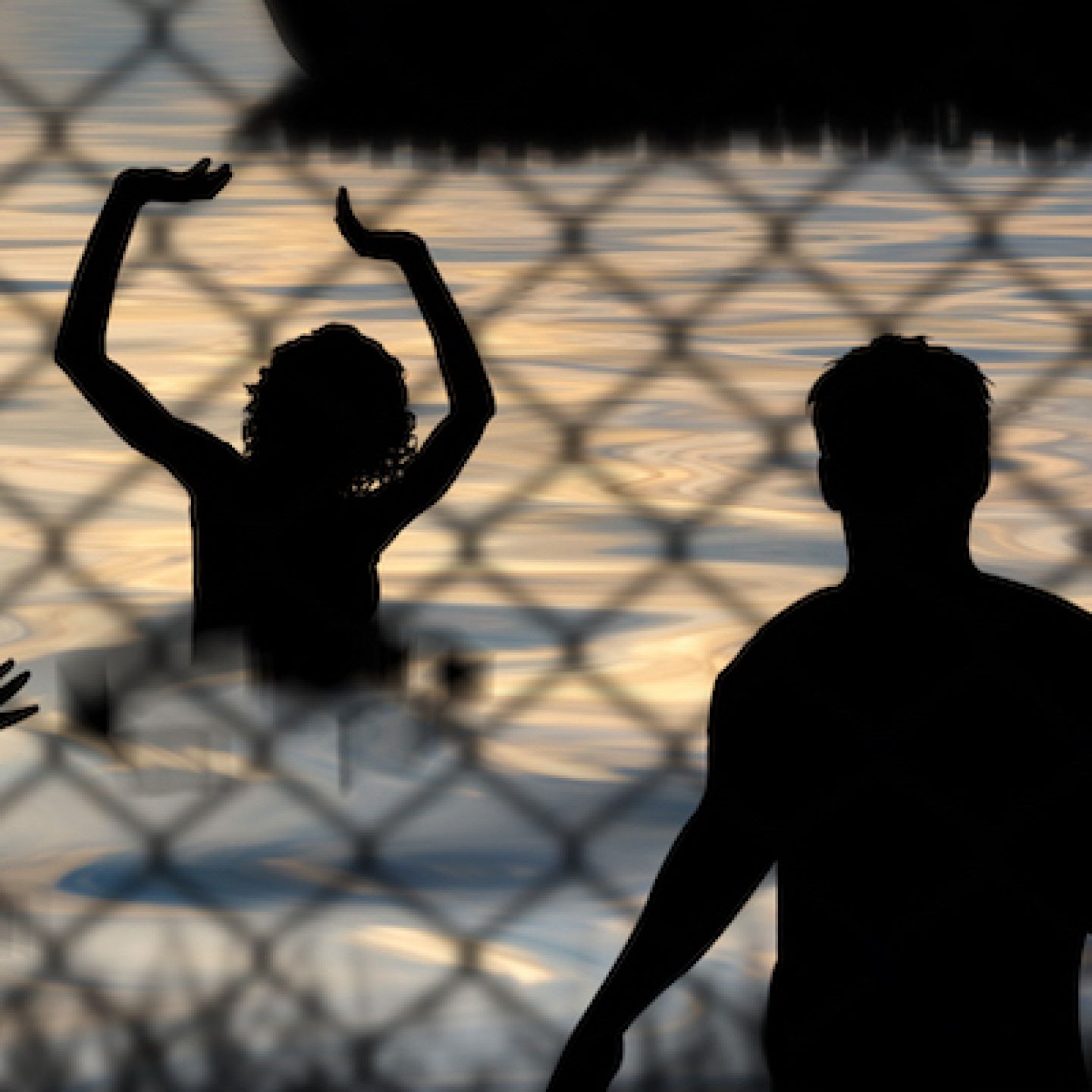 Refugees swim to shore against the backdrop of a chain wire fence