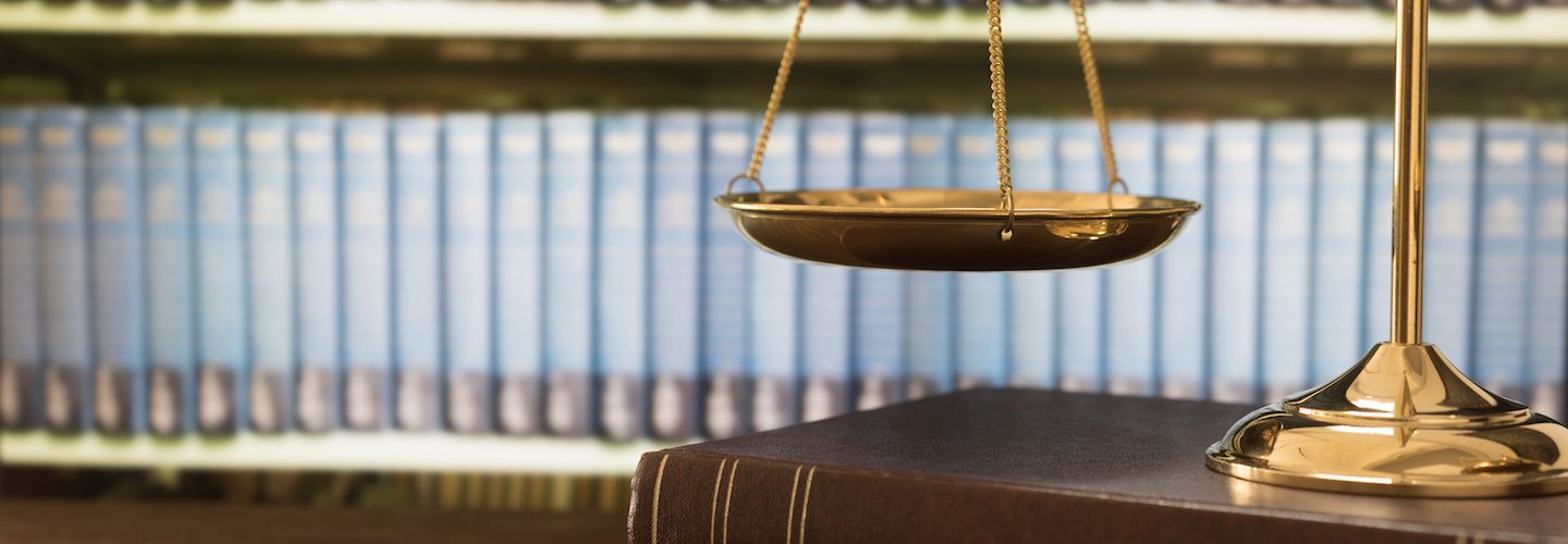 Scales of justice pictured in front of a shelf of books in the library of a law firm