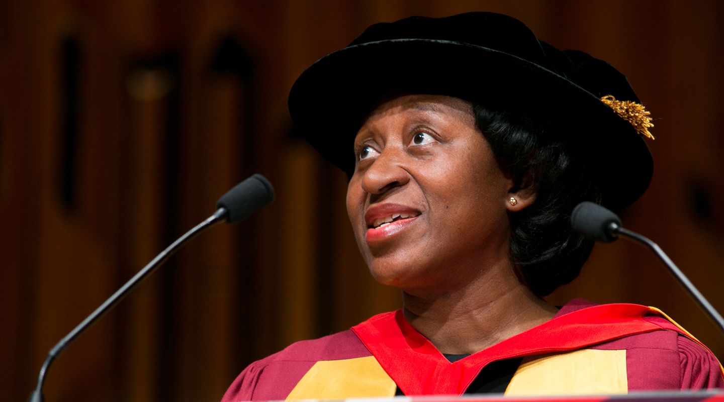 Judge Barbara Mensah, a black woman in graduate cap and gown, talking on a podium at a graduation ceremony.