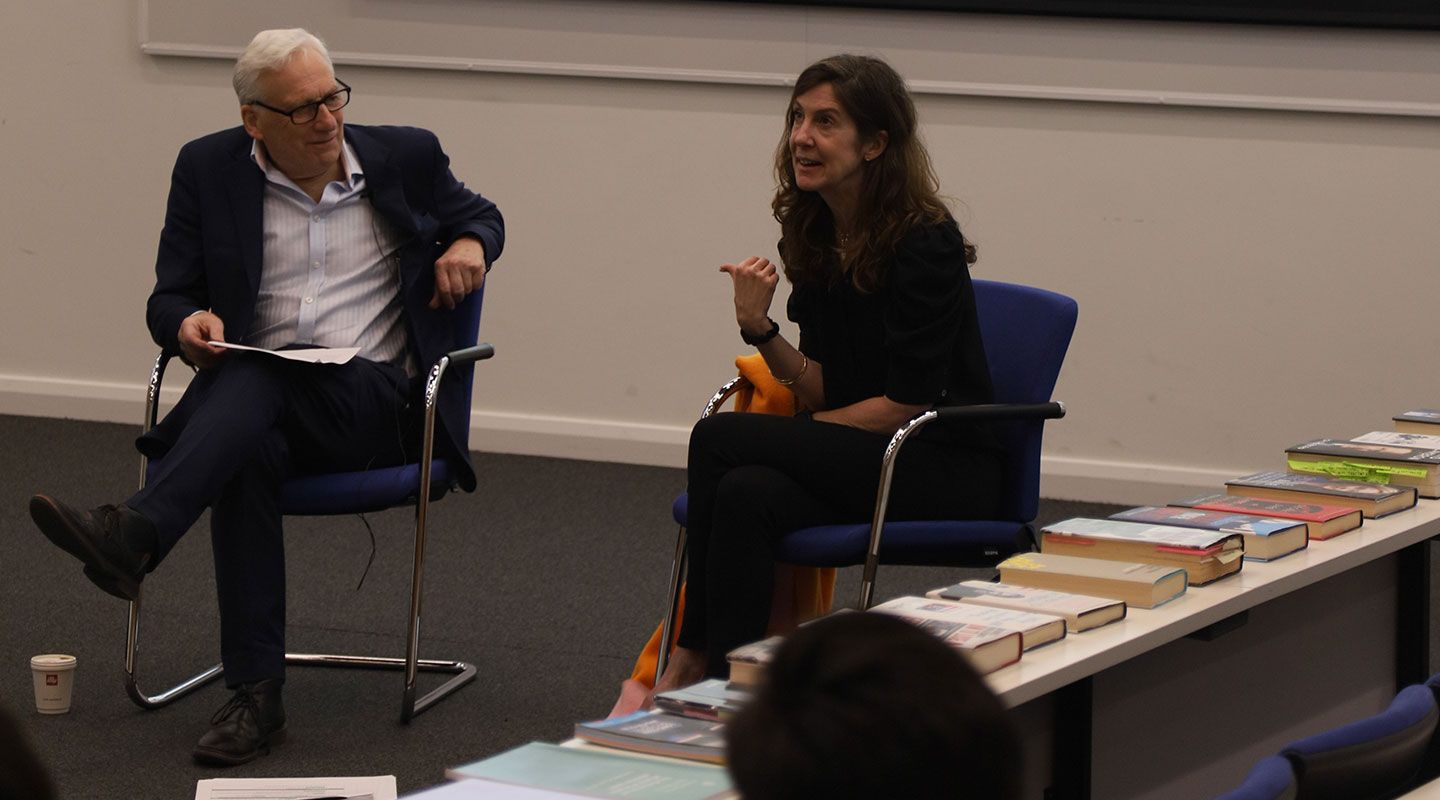 Professor Barney Jones of City's Journalism Department (left) and Esme Wren (Channel 4 News) sit on chairs. To Esme's right is a row of policial books on a desk