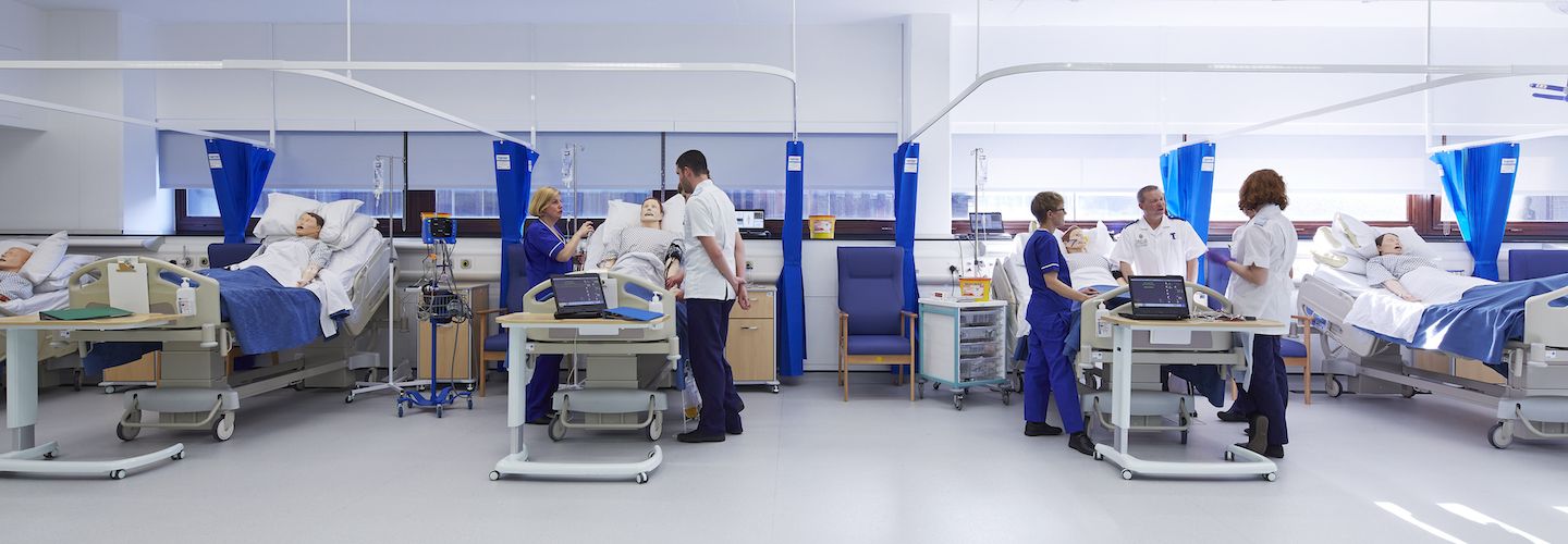 Nurses standing next to patients in beds in the clinical suite