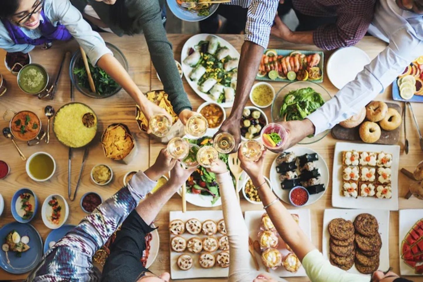 Overhead image of people joining glasses over a table full of food.