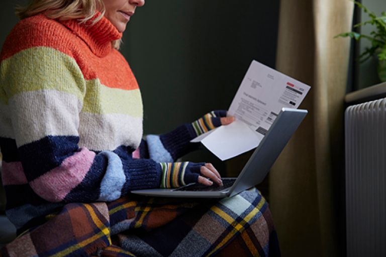 Woman in a sweater trying to pay a bill on a laptop.