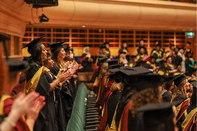 City graduates clapping at their graduation ceremony wearing their robes and mortarboards at the Barbican Centre