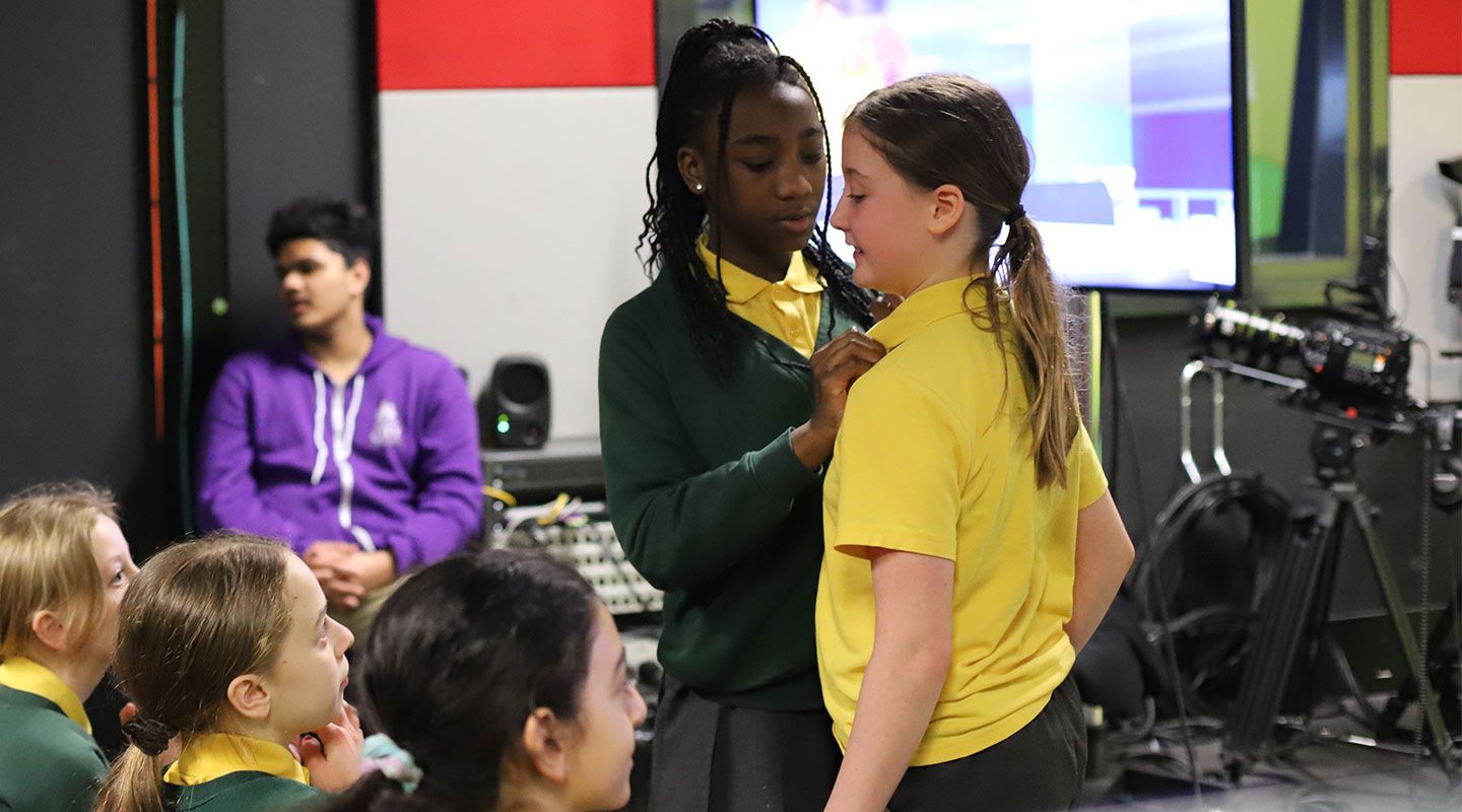 A pupil helps another put on a microphone at City's broadcast studio