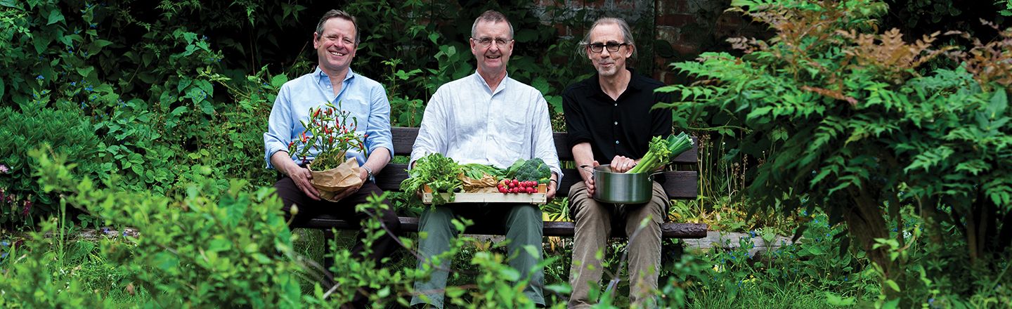 Professors Tim Lang, Martin Caraher and Dr David Barling sitting on a bench holding vegetables in a park