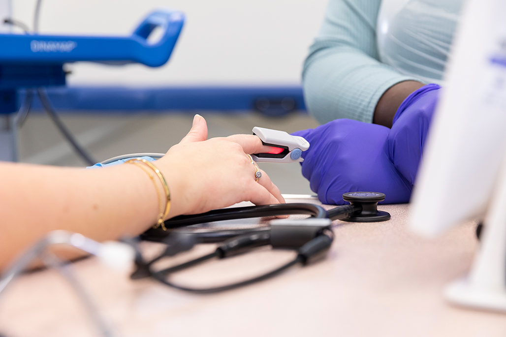 Student wearing gloves taking blood pressure measurement using participants finger