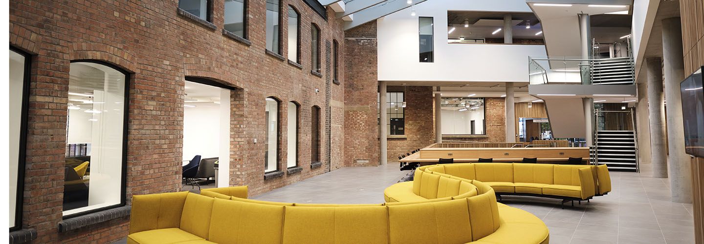 Internal of Law School Building at ground floor level looking at yellow sofas and exposed brick walls.