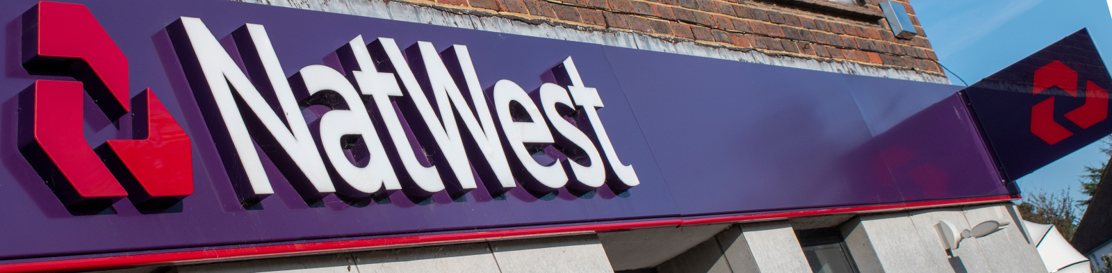 Man walks past a NatWest bank branch and cash machine
