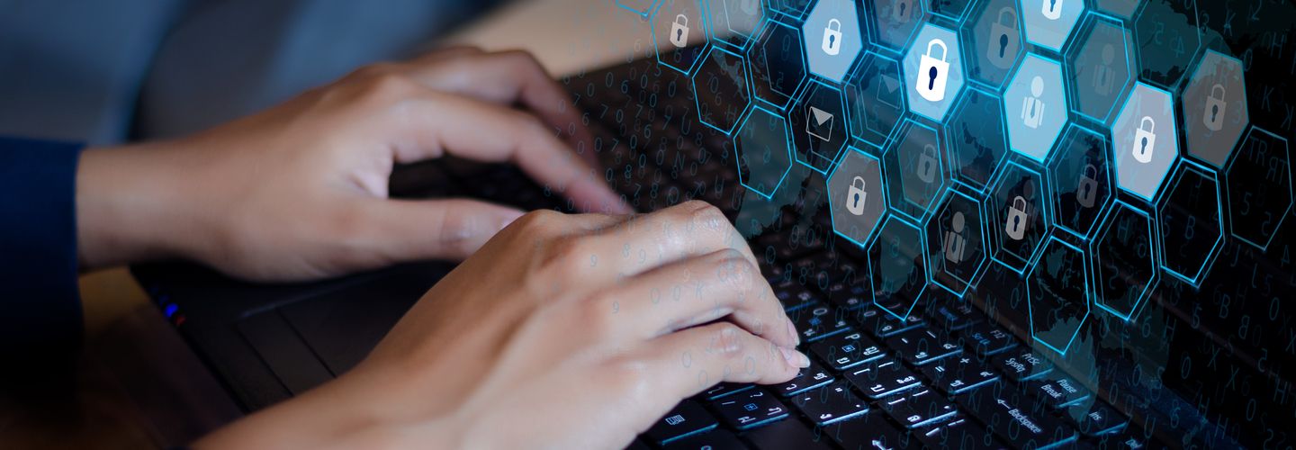 A woman's hands typing on a laptop with cyber security hexagonal graphics illustrated over its screen with a padlock image contained with each hexagon.