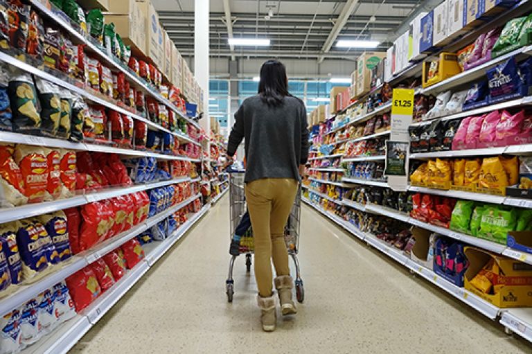 Woman walking a shopping trolley down a supermarket aisle