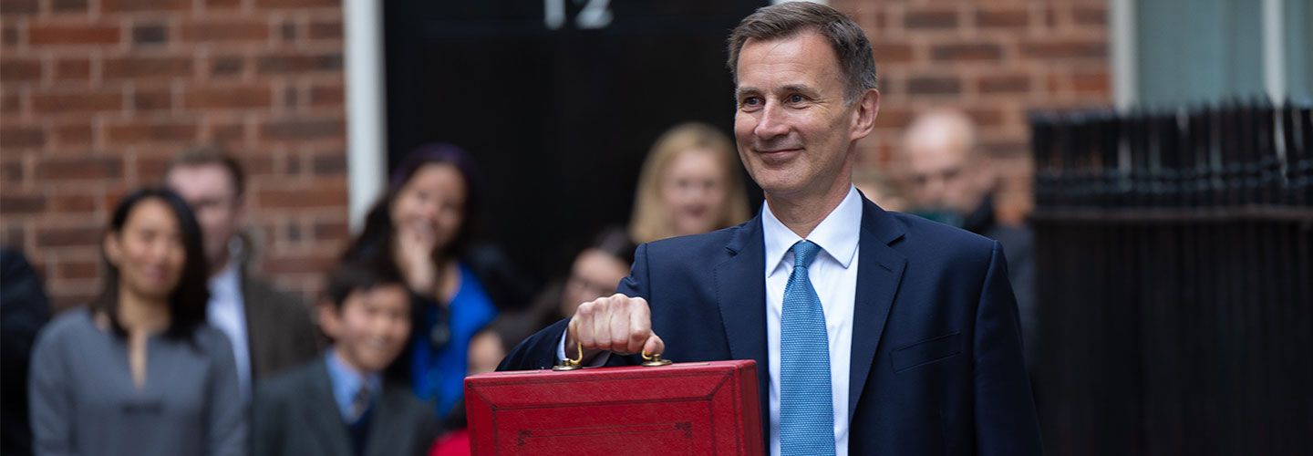An image of Jeremy Hunt, Chancellor of the Exchequer, stands in front of Downing Street holding out the red box briefcase which holds the budget.