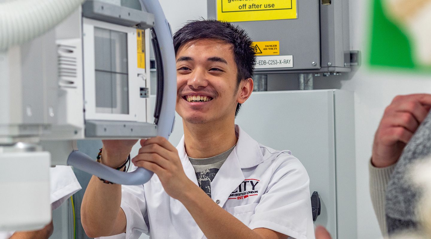 A male first year, radiography student smiles happily while using the xray equipment.