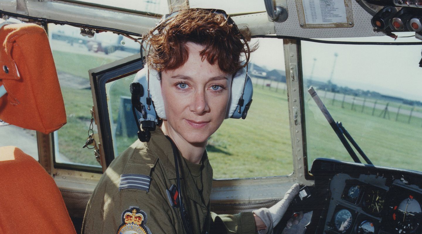 Julie Gibson, a young white woman with short curly brown hair, in RAF uniform and headset, seated in the cockpit of an RAF aircraft.