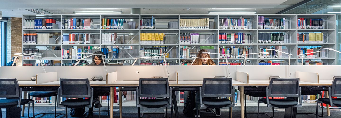 Two female law students sitting in individual study spaces in front of shelves full of books