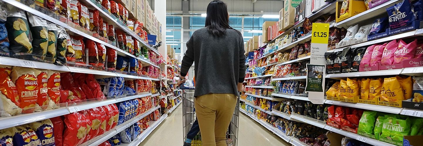 Woman walking a shopping trolley down the aisle of a supermarket