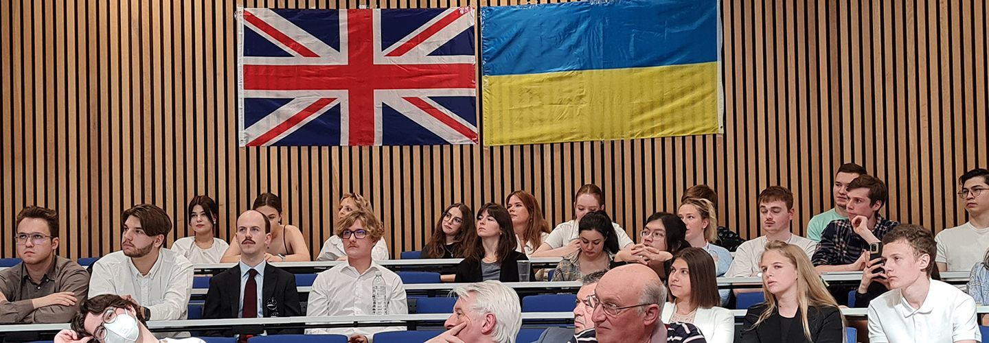 Audience of students and staff with Union Jack and Ukraine flags on the wall.