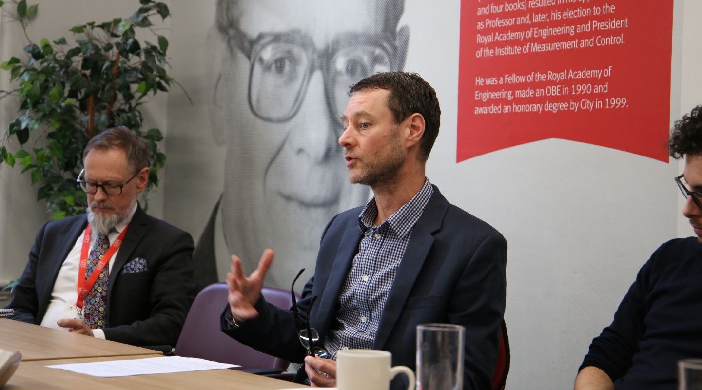 Male academic sitting on a panel speaking to a group of people.