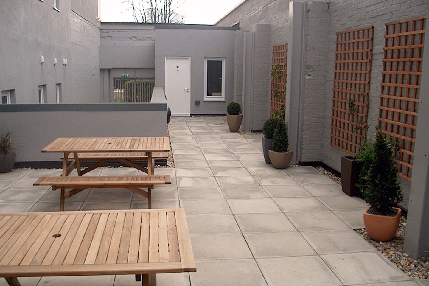 Private paved courtyard with two picnic tables, pot plants and trellises.