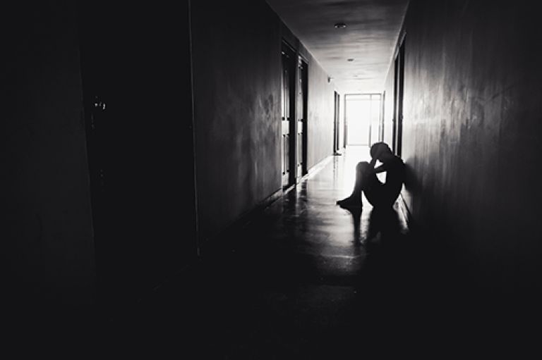 Black and white image of a silhoutted person sitting in a corridor with their head in their hands