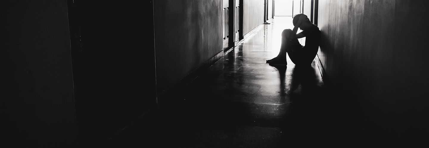 Black and white image of a silhoutted person sitting in a corridor with their head in their hands