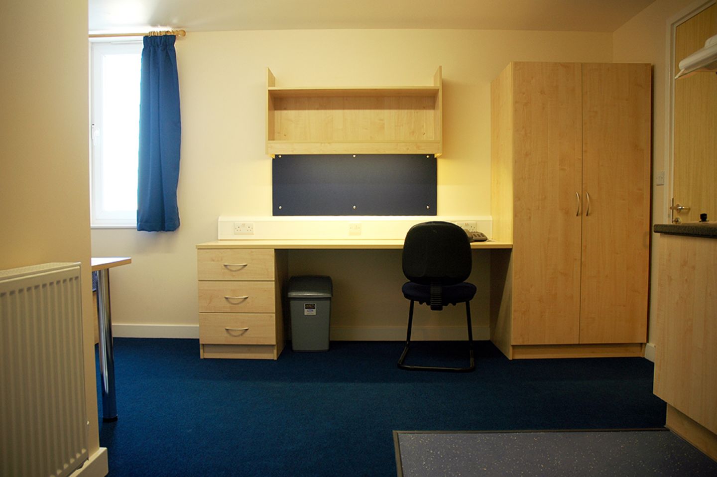 View of a studio room showing the wide desk and wardrobe. There is also a radiator visible facing the kitchen area.