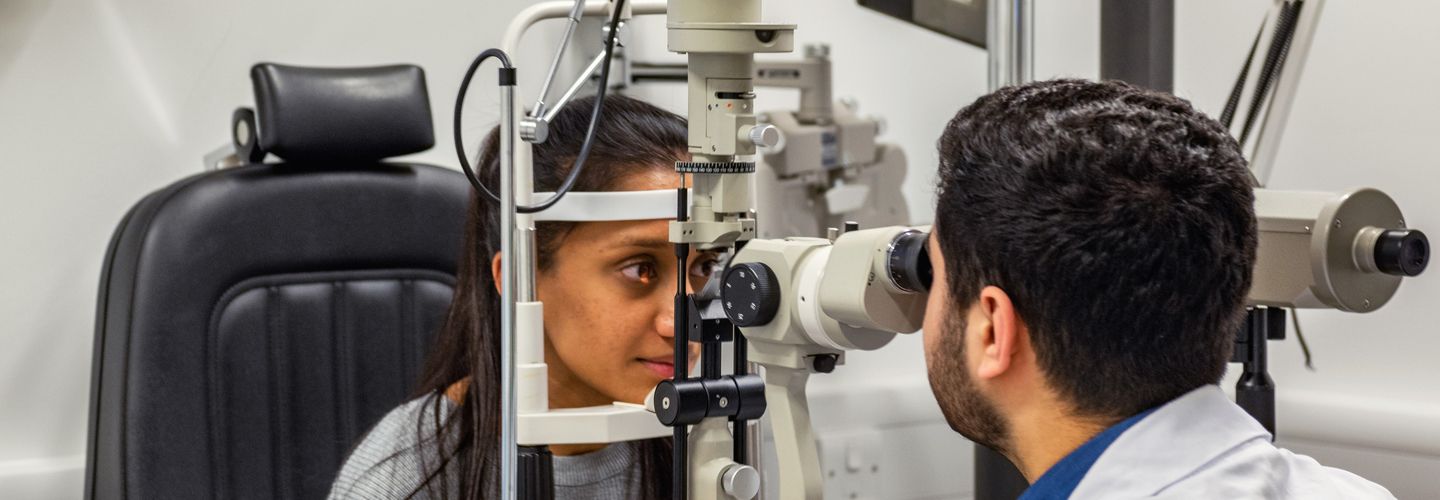 Male optician uses diagnostic equipment to examine female patient's eyes.
