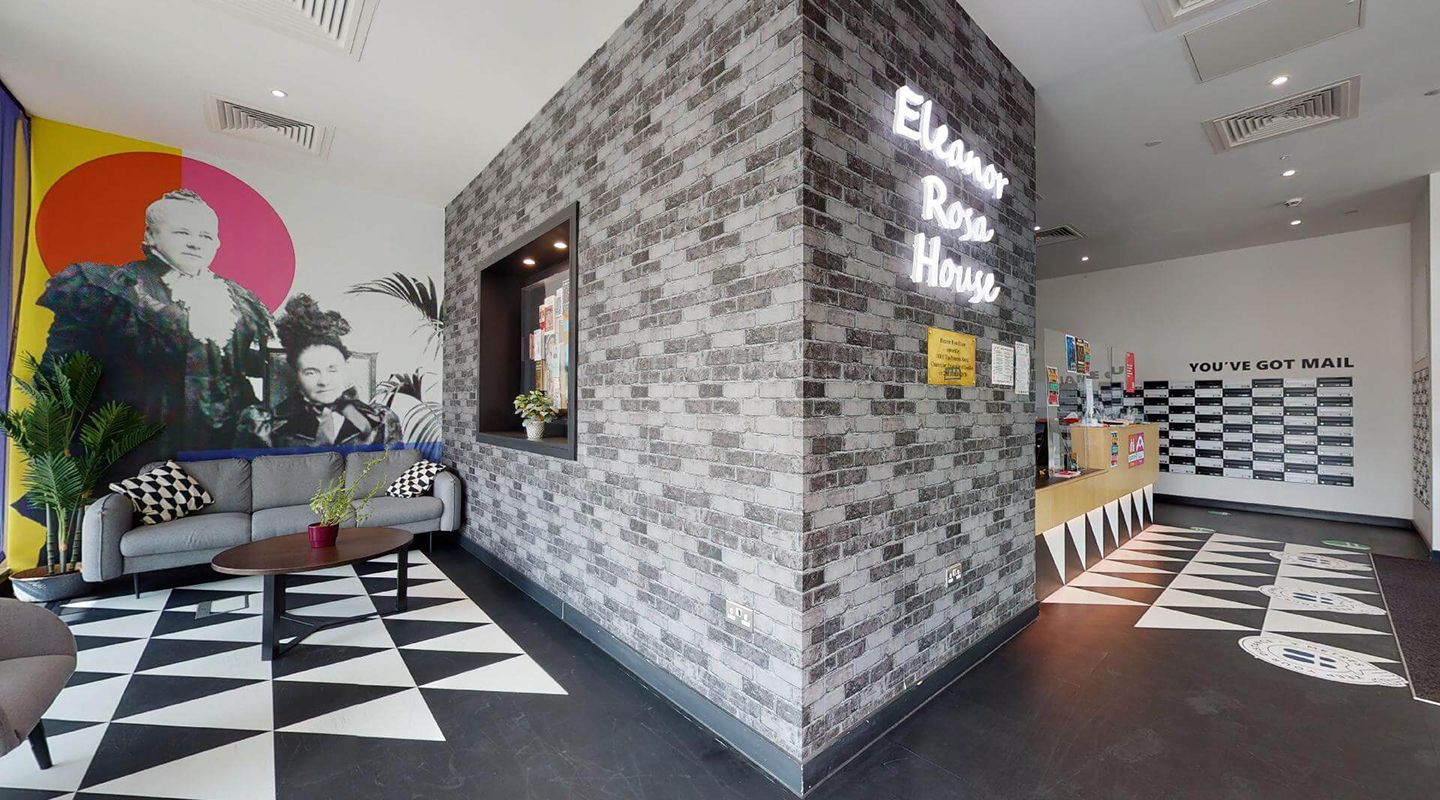 Reception lobby with bright wall art sofa, reception desk and post boxes in a white and black colour scheme. The name of the House is in florescent lights on a grey brick dividing wall which also features an inset notice board.