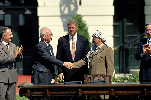 Yitzhak Rabin and Yasser Arafat shake hands in front of Bill Clinton.